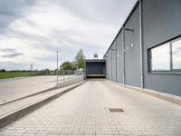 brick walkway next to grey building with white doors and window overlooking grassy field area below