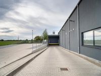 brick walkway next to grey building with white doors and window overlooking grassy field area below