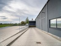 brick walkway next to grey building with white doors and window overlooking grassy field area below