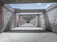 a long hallway lined with concrete walls and windows and light posts and beams above it