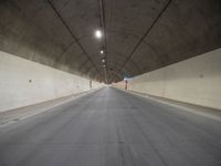 an empty street inside a big tunnel that is surrounded by cement walls and two people on bikes