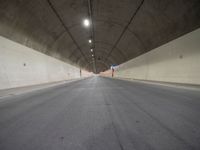 an empty street inside a big tunnel that is surrounded by cement walls and two people on bikes