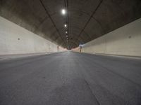 an empty street inside a big tunnel that is surrounded by cement walls and two people on bikes