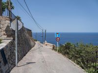 a paved road with a warning sign and a railing near the ocean that goes to the shore