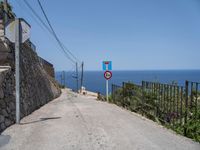 a paved road with a warning sign and a railing near the ocean that goes to the shore