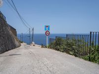 a paved road with a warning sign and a railing near the ocean that goes to the shore