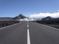 a road leads through an arid area in front of a mountain range and cloudy skies