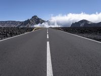 a road leads through an arid area in front of a mountain range and cloudy skies