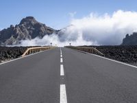 a road leads through an arid area in front of a mountain range and cloudy skies