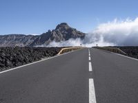 a road leads through an arid area in front of a mountain range and cloudy skies