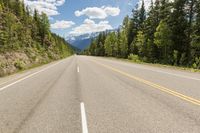 a straight mountain road with mountains in the distance and trees growing on the side of it