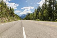 a straight mountain road with mountains in the distance and trees growing on the side of it