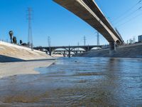 a large bridge over a creek next to power lines and water filled with floodwater