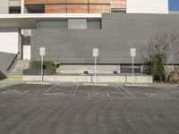 an empty parking lot in front of a gray and white building with some signs in it