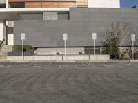 an empty parking lot in front of a gray and white building with some signs in it