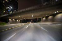 a road that has some cars driving on it with buildings behind it with lights on