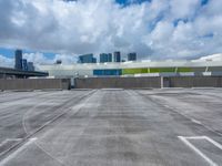 the sky is full of fluffy clouds and buildings in the background with an empty parking lot