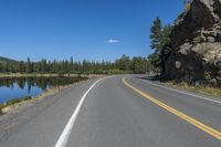 an empty road is next to some water in the mountains near a lake with some trees