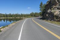 an empty road is next to some water in the mountains near a lake with some trees