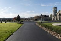 a view of an old stone building, grassy lawn, and a pathway with a clock tower on it