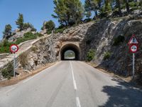 a tunnel leading into the mountains near some trees and road signs showing no left turn