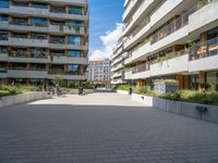 the paved walkway leads into an outdoor courtyard in urban city setting at daytime with people sitting on benches