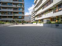 the paved walkway leads into an outdoor courtyard in urban city setting at daytime with people sitting on benches