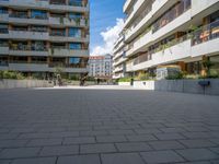 the paved walkway leads into an outdoor courtyard in urban city setting at daytime with people sitting on benches