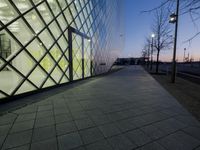 a sidewalk is next to the building and a lamp post are at dusk in winter