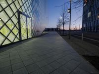 a sidewalk is next to the building and a lamp post are at dusk in winter