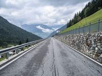 a long road lined with rocks next to a fence with a few cars driving along it