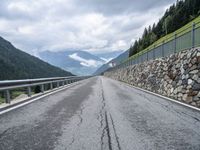 a long road lined with rocks next to a fence with a few cars driving along it