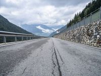 a long road lined with rocks next to a fence with a few cars driving along it