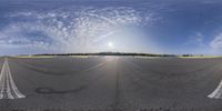 a fisheye lens view of an asphalt road with a sun and blue sky in the background