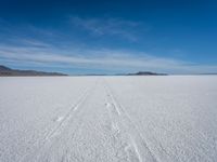 two tracks on the snow on a large plain with mountains and ocean in the background