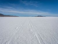 two tracks on the snow on a large plain with mountains and ocean in the background