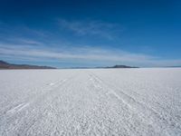 two tracks on the snow on a large plain with mountains and ocean in the background