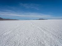 two tracks on the snow on a large plain with mountains and ocean in the background