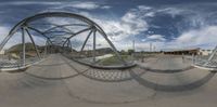 a fisheye lens looking up at the bridge and walkway over it, with clouds above