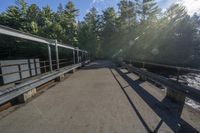 sunlight shines on the road near a bridge and river with metal railings over it