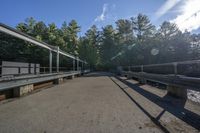 sunlight shines on the road near a bridge and river with metal railings over it