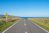 a road leading to the ocean with a stop sign at either end of it and grass growing on the sides