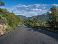 the road winds up on the mountainside on a sunny day with beautiful clouds and trees