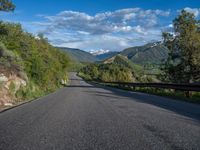 the road winds up on the mountainside on a sunny day with beautiful clouds and trees