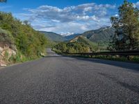 the road winds up on the mountainside on a sunny day with beautiful clouds and trees