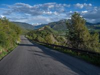 the road winds up on the mountainside on a sunny day with beautiful clouds and trees