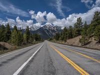 road in the mountains with pine trees and mountains in the background with blue sky with fluffy clouds