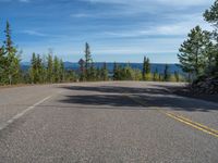 the mountains are visible in the distance from this wide, empty road, overlooking a wide landscape and forest