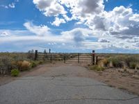 a gate is at the side of the road with clouds above it and a blue sky above