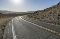 a motorcycle riding down a winding highway between hills and dry grass on a sunny day